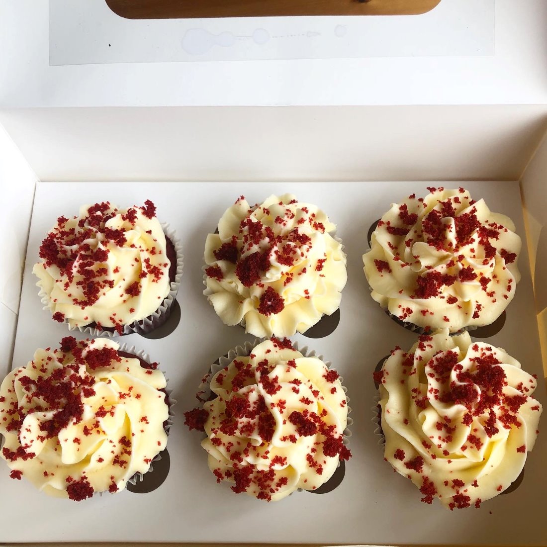 A box of six red velvet cupcakes piped with cream-cheese frosting and red velvet crumb